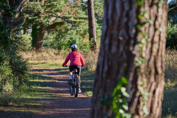 Naklejka premium nice senior woman cycling with her electric mountain bike in a pine tree forest