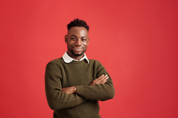 Portrait of African American man wearing green sweater and white collared shirt, smiling confidently with arms crossed against vibrant red backdrop