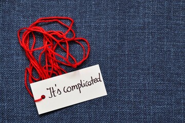 A photo illustrating the saying that it's complicated; Red thread with the handwritten inscription 'it's complicated' on a navy blue background