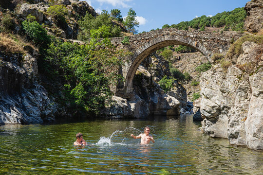 Young adults bathing and having fun in a river at old Genoese bridge in Asco, Corsica