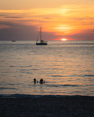 Beautiful sunset at Porto de Piana, Corsica. Silhouette of sailboat and people bathing in sea