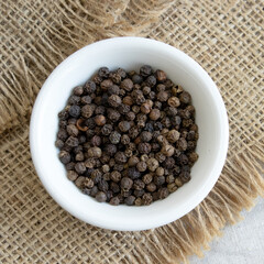 Pile of Black peppercorns Black pepper dried seeds in wooden spoon on linen background