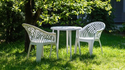 A set of white plastic patio furniture, including stackable chairs and a small table, set up in a grassy backyard.