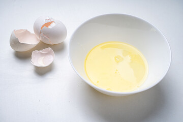 Raw egg white in a white bowl on the table and eggshells.