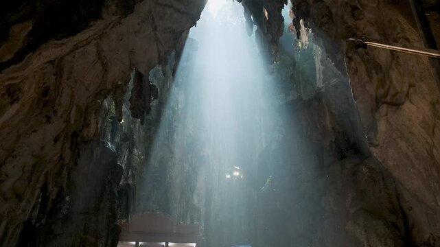 Batu Caves interior, Selangor, Malaysia. Tourists visiting Batu cave complex illuminated staircase with people by natural light streaming through the cave's opening, Kuala Lumpur. Travel landmark