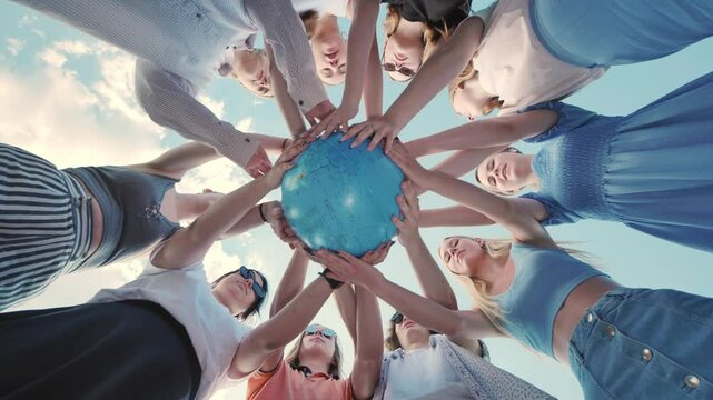 Group of young people are standing in a circle holding a globe with their hands, united for the future of the planet.