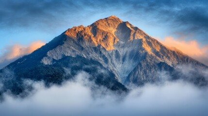 A majestic mountain peak rises above swirling clouds, bathed in warm sunlight, highlighting its rugged terrain and captivating beauty.