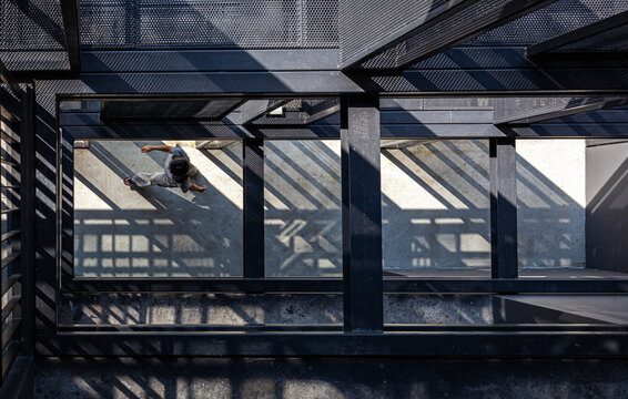 Architecture details of view from top through the steel columns and beams structure with a woman walking across in the strong light and shadow.