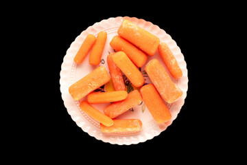 Small peeled carrot with ceramic dish on black background, macro, top view.