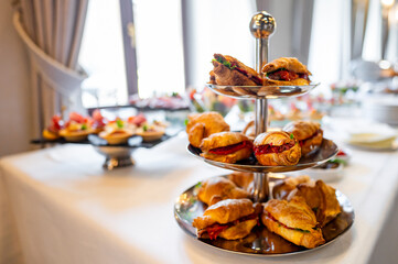 Three-tiered serving tray with assorted pastries and finger foods on a table. Blurred background. Ideal for high tea, catering, or culinary presentations. Perfect for food and beverage photography.