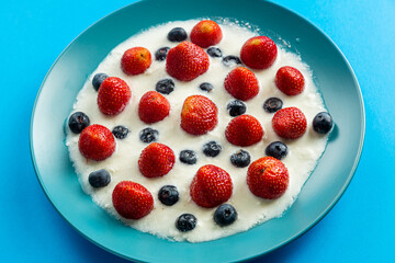 Berries juicy strawberries and blueberries in a blue plate with cream on a blue background