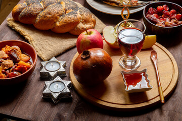 Challah, honey, apple and pomegranate and wine and chelnt on the table with menorah and burning...