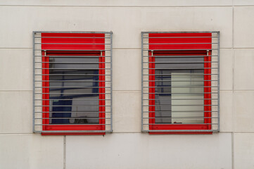 Two windows with red frames are protected by metal bars