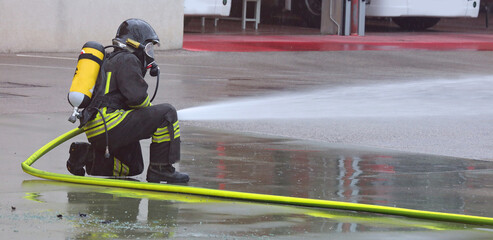 firefighter in action with an oxygen tank and respirator deploying extinguishing agent during an...