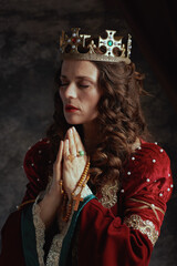 medieval queen in red dress with rosary and crown praying