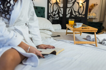 Pretty girl in the hotel room with bathrobe chilling and reading a book.
