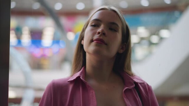 Lady in unbuttoned pink dress relaxes with a gentle smile on her face as the elevator goes up, the background features blurred elements and colorful bokeh lights, seen through the glass