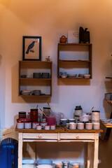 A ceramic workshop featuring shelves filled with pottery, a pottery wheel, glass jars and pictures