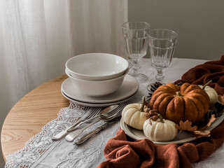 Seasonal autumn table setting - a plate with decorative pumpkins, cones, dishes, glasses on a round wooden table