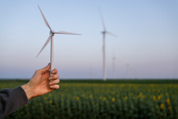 Man holds toy wind turbine in his hand. Real wind turbines in the background