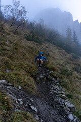 Fototapeta premium Boy in blue jacket hiking a steep mountain trail in misty weather. Concept of outdoor adventure, exploration, and active childhood in nature. High quality photo