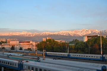 Almaty city skyline. Buildings and mountains illuminated by the setting sun. Railway station.