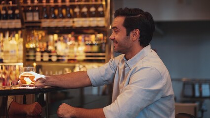 Smiling smart man drinking cocktail in Old fashioned with enjoy in cheers with friends or stranger sitting across special vibrant beverage at nightclub on Friday meeting at luxurious bar. Vinosity.