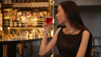 Sitting beautiful drinking alone in Cosmopolitan red cocktail waiting friends or couple at bokeh lighting luxurious beverage counter nightclub at pub and restaurant on Friday meeting night. Vinosity.