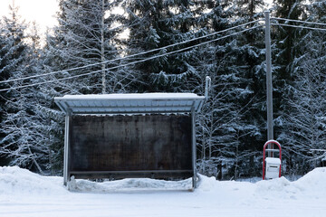An empty bus stop against the backdrop of a snow-covered forest