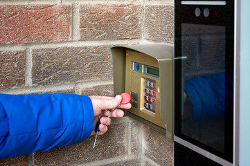 A person using a key fob to access a building via a keypad entry system mounted on a brick wall