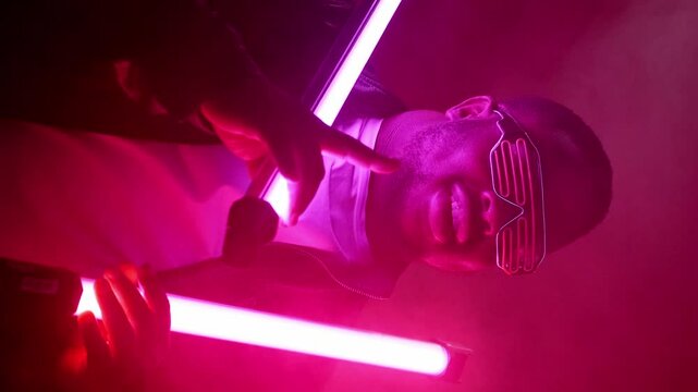 Vertical video. Rap show. Nightclub performance. Cool stylish confident joyful man in trendy sunglasses singing at hip hop event stage on bright neon lamp light smoke background.