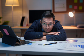 Exhausted businessman lying on his desk at night in office, feeling tired and stressed from working with financial documents