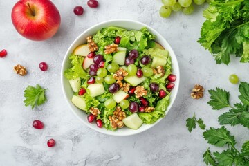 A white bowl of fresh salad with mixed greens celery apple pomegranate seeds and grapes topped with walnut dressing viewed from above