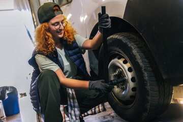 Young ginger woman mechanics repairing the wheel of a truck, combi, long vehicle.