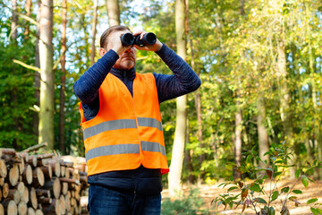 Logging engineer inspector in uniform looks through binoculars and controls forest cutting. Male...