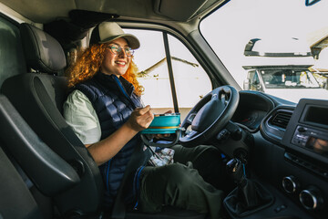 Ginger woman truck driver taking a break from long drive to eat some food from container.