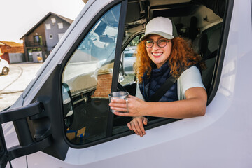 Young ginger woman driving long vehicle and drinking coffee so she could get some energy.