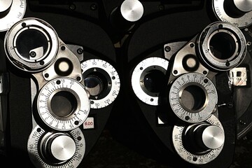 Front detail of vintage manual mechanical phoropter device, optical tool used by optometrist to determine patients refractive eye errors such as myopia or hyperopia, sunlit by bright afternoon sun.