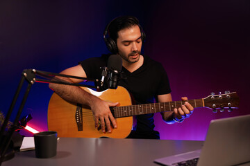 Obraz premium Host channel of smart influencer in creative audio on live streaming to fanclub with sing with play guitar music blogger using headset and mic social media online at neon light modern studio. Surmise.