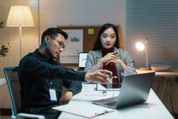 Two business people working late in the office, brainstorming and discussing over a laptop