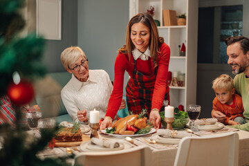 Woman serving christmas turkey to family at decorated table