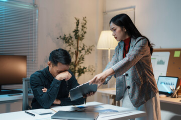 Businesswoman pointing at document while blaming businessman for mistake at night in the office