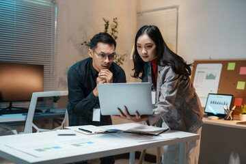 Two business people looking concerned while working late on a laptop, struggling to meet a deadline