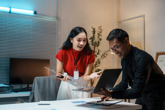 Young asian business people working late looking at laptop and having fun in office at night - Powered by Adobe