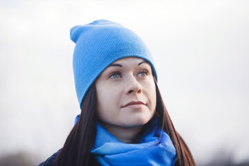 A woman wearing a blue hat and scarf is looking off into the distance