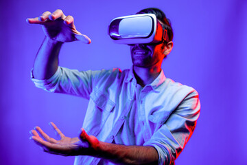 Caucasian smart man holding and moving gesture while using VR goggle. Happy person using headset and goggle while enter virtual world or metaverse with neon light background. Technology. Deviation.