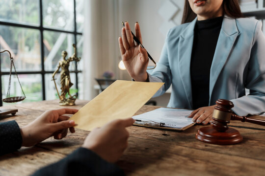 Lawyer is refusing an envelope offered by a client, with a scale and gavel in the background