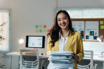 Young asian businesswoman holding a stack of paperwork and smiling in a modern office