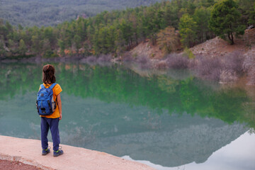 Naklejka premium summer camp. a boy with a backpack looks at a beautiful mountain lake. trekking near a mountain lake.