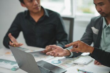 Business team having a discussion and analyzing data on a laptop while pointing at financial charts during a meeting